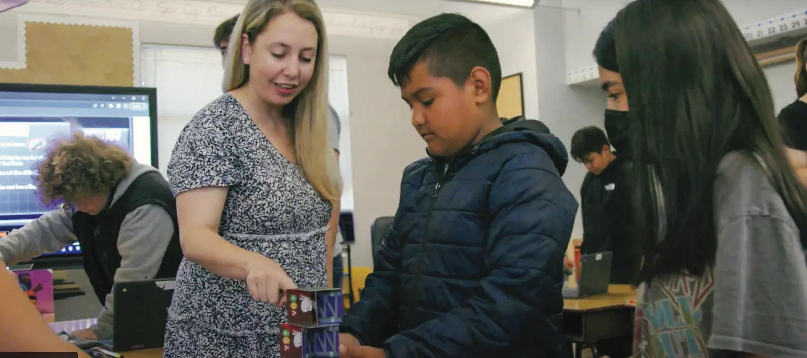 A teacher leans in to observe a group of students working through a collaborative challenge